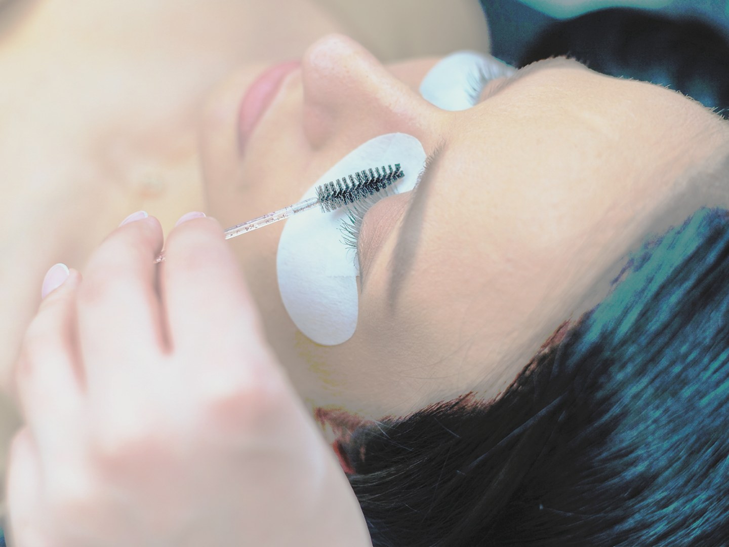 Wimpernlaminierung: weisse Pads unter dem Auge und schwarze Bürste beim Formen der Wimpern